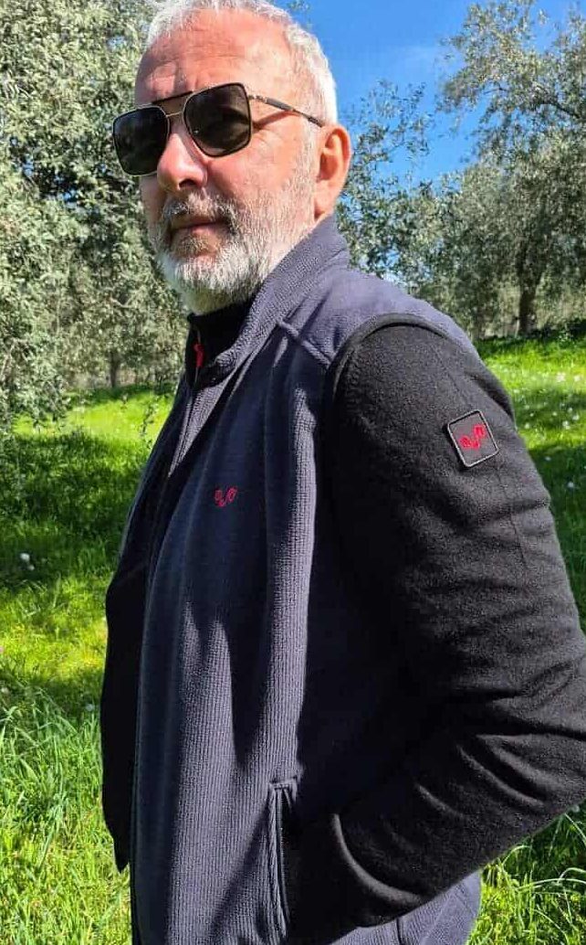 Άνδρας με ζακέτα και γιλέκο από μαλλί merino απολαμβάνει τη βόλτα του στον ήλιο, επιλέγοντας ποιοτικά outdoor ρούχα για πεζοπορία και δραστηριότητες στη φύση.