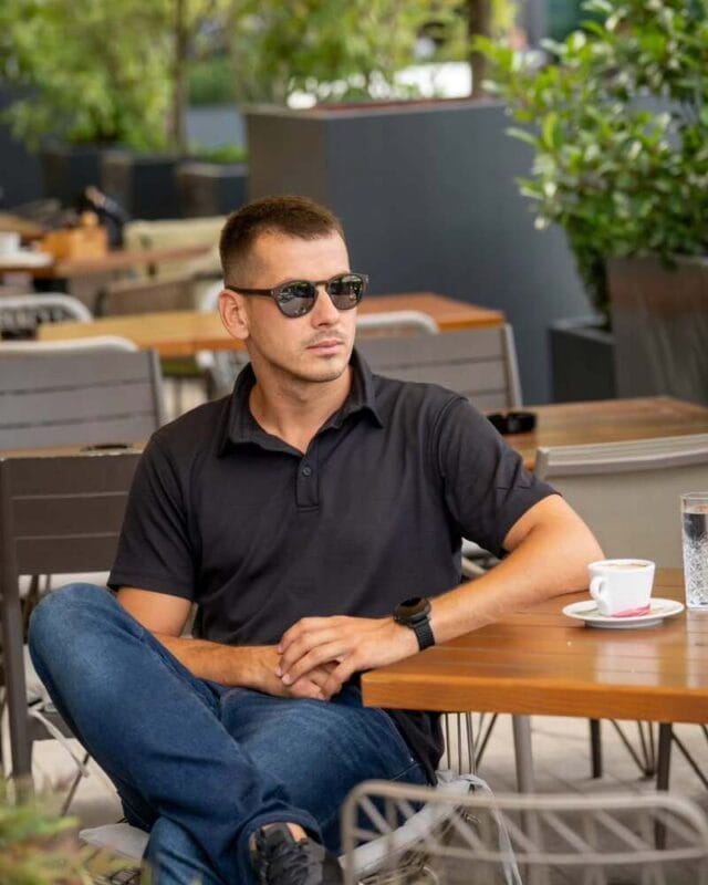 Άνδρας που φοράει μαύρο polo από 100% merino wool και πίνει καφέ στην πόλη, μια κορυφαία επιλογή για αντιιδρωτικά μπλουζάκια το καλοκαίρι.